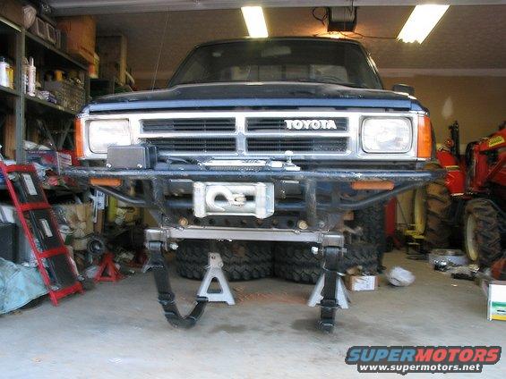Front view of a dark blue Toyota truck on jack stands, with a winch mounted on the aftermarket bumper