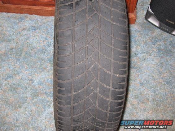 Close-up of a tire with a geometric tread pattern, resting on a carpeted floor