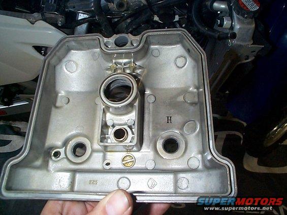 Motorcycle engine valve cover with visible 'H' marking and bolt holes