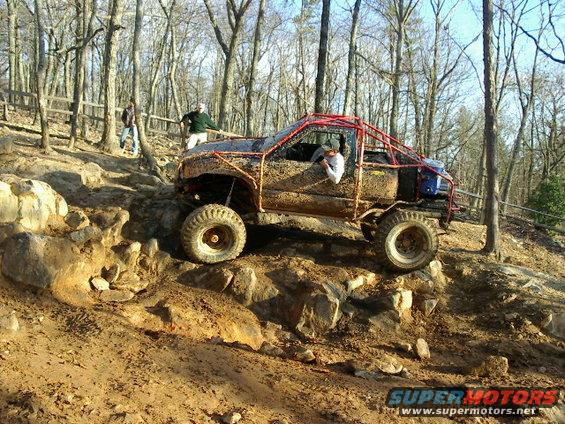 Muddy off-road truck with roll cage climbing rocks