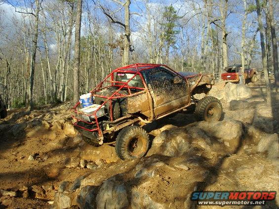 Modified off-road buggy with roll cage climbing over rocks, another vehicle visible behind