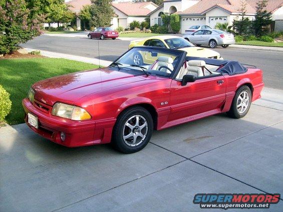 Red convertible with white interior, 5.0 badge on fender, parked on driveway
