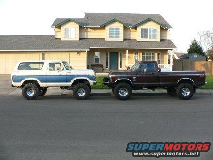 White and blue Bronco and brown pickup truck parked on street in front of house