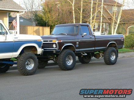 Brown 1979 Ford F-250 pickup truck, lifted with large tires, parked next to a white and blue truck