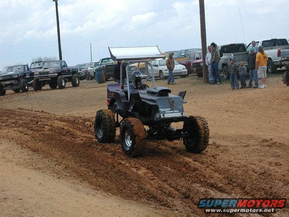 Custom mud bogger with large tires and a spoiler driving through mud