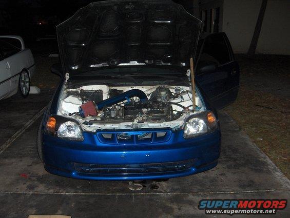Blue Honda Civic, hood and driver door open, engine exposed. Another car is parked to the left