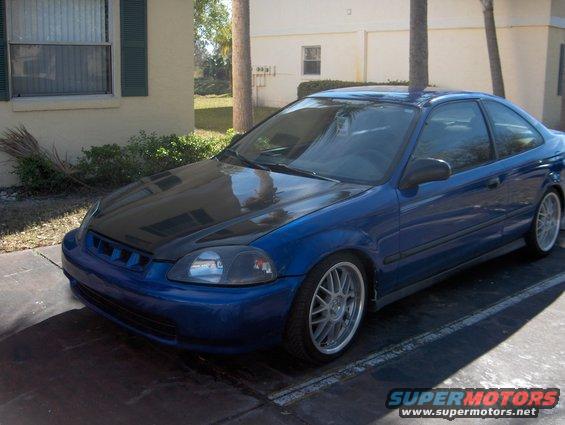 Blue coupe with black hood, aftermarket wheels, parked outdoors