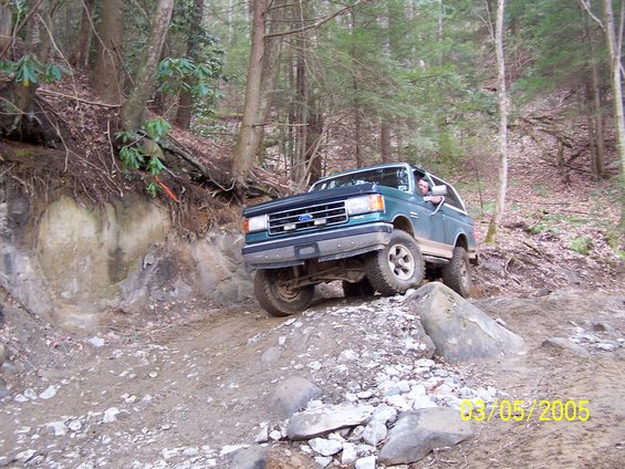 Green Ford Bronco climbing a rocky trail in the woods. Date stamp reads 03/05/2005