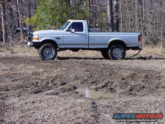 White pickup truck with a toolbox in the bed, parked in a muddy area with trees in the background