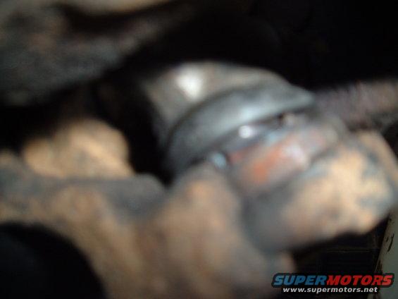 Close-up of a dirty, metallic vehicle suspension part with orange accents