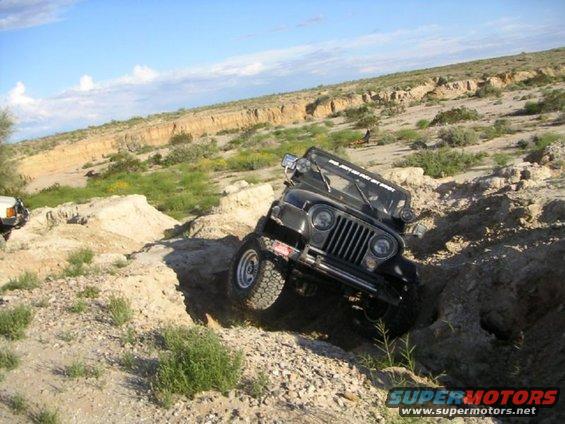 Black Jeep CJ-7 navigating a rocky off-road trail, another white vehicle visible in background