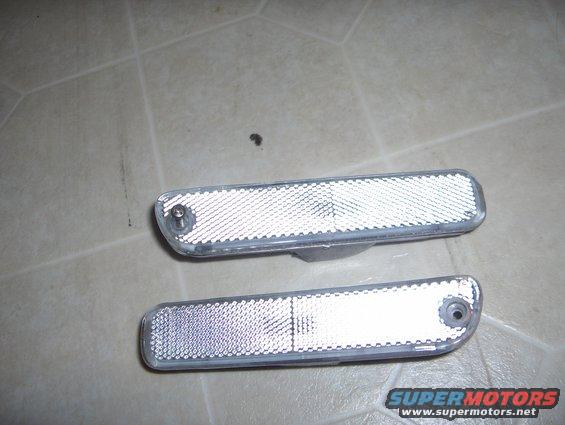 Two clear plastic car side marker lights with reflective backing on a tiled floor