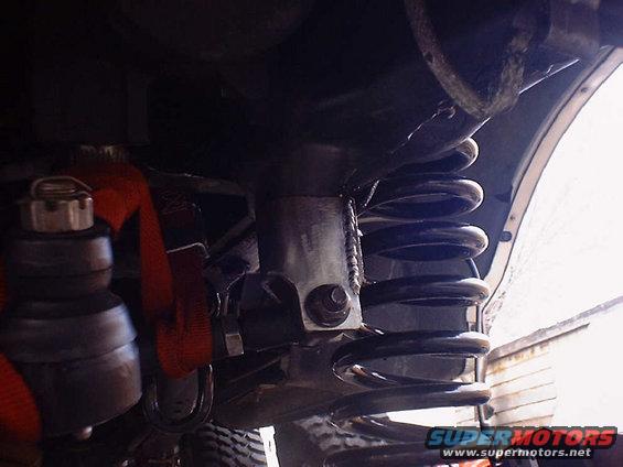 Close-up of a vehicle's coil spring and suspension linkage, with a red strap visible