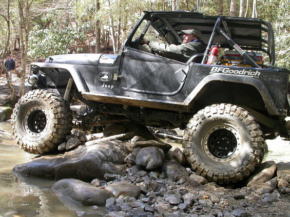 Black Jeep Wrangler off-roading over rocks and water, BFGoodrich tires visible
