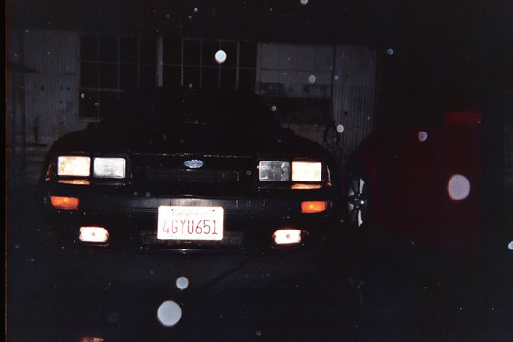 1985 Ford Mustang front view at night, license plate 4GYU651, parked next to a red car