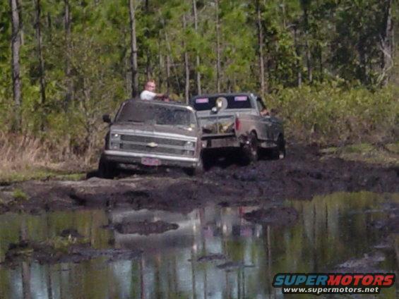 Mud-covered Chevrolet C/K pickup truck stuck in mud, with a Ford F-Series pickup truck behind it