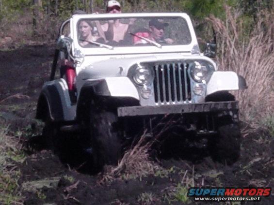 White Jeep CJ-7 with people inside driving through mud, front view