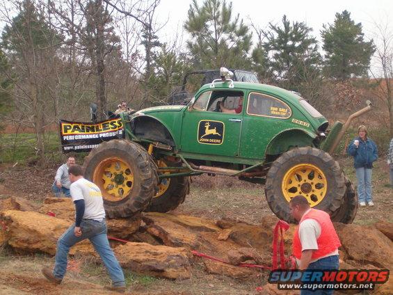 Green off-road Volkswagen Beetle with John Deere logos and oversized tires navigating rocks