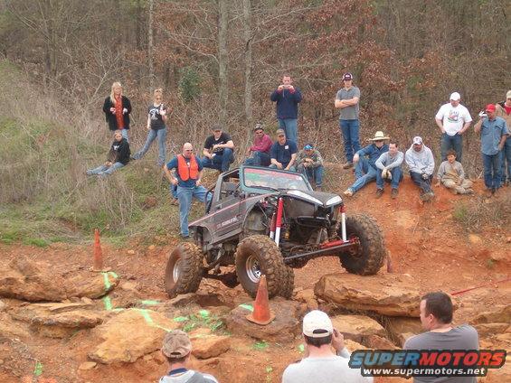 Off-road vehicle with large tires and exposed suspension climbing rocks