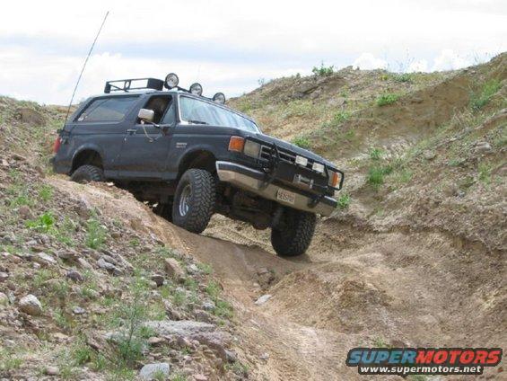 Dark Ford Bronco climbing a dirt hill with roof lights and a brush guard