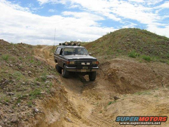 Dark SUV with roof lights driving on a dirt trail, front-right tire lifted