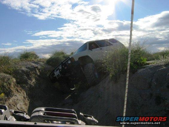1988 Ford Bronco climbing a steep dirt hill, another vehicle visible in foreground