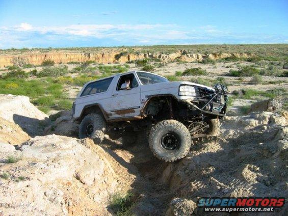 White off-road SUV with large tires navigating rocky terrain