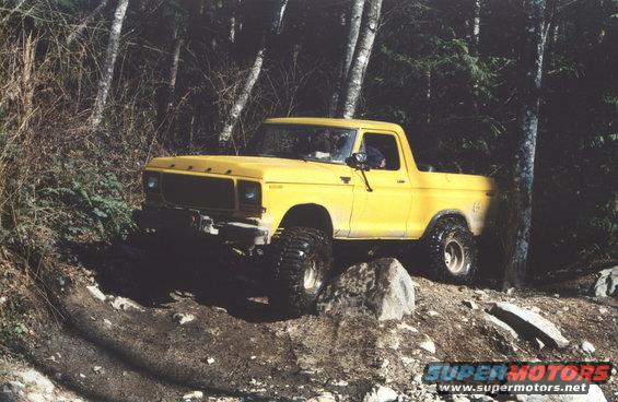 Yellow pickup truck with large tires driving on a rocky, wooded trail
