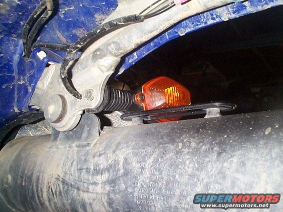 Close-up of a motorcycle's orange turn signal and wiring, with some text visible on a part below