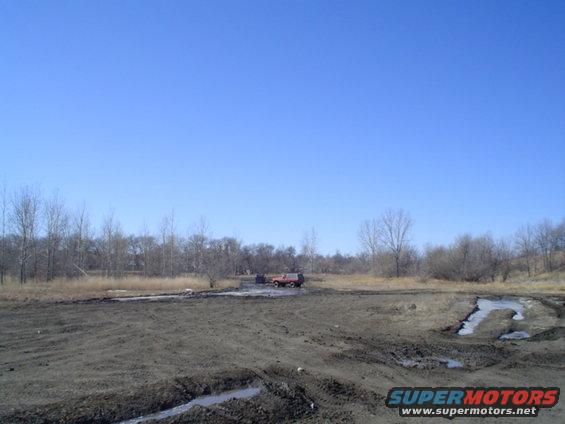 red SUV stuck in a muddy field with trees in background