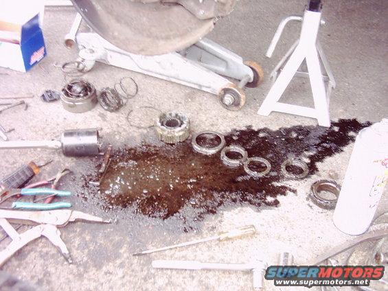 Vehicle wheel hub and bearings disassembled on the ground with tools and a jack stand