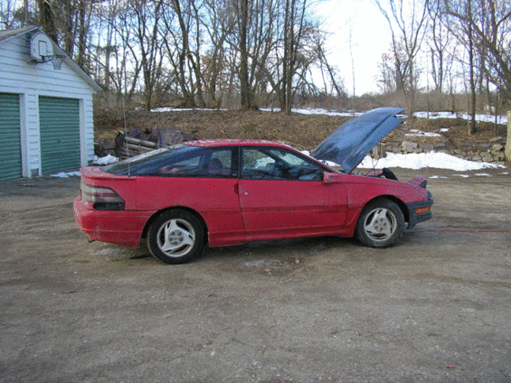 red hatchback car with hood open, parked outside near a building