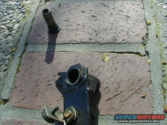Close-up of a black metal automotive part with a hollow cylinder on a brick surface