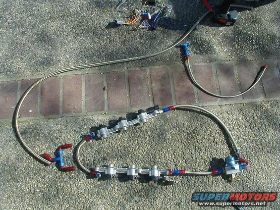 Fuel rail system with braided lines and blue/red fittings on paved ground