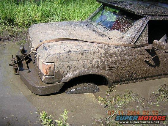 Mud-covered 1990 Ford Bronco stuck in mud, front 3/4 view