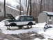 1994 Ford Bronco - A two-tone green and white Ford Bronco is elevated on jack stands in a snowy driveway, with its hood open.