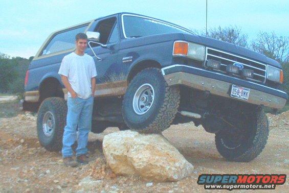 1989 Ford Bronco with a person standing next to it, one tire on a rock