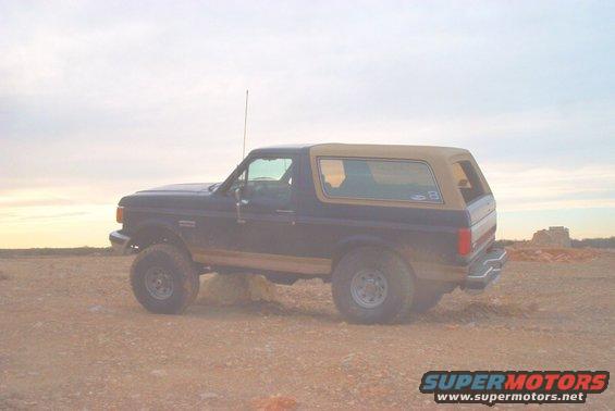 Side view of a dark blue and tan Ford Bronco parked on a dirt lot