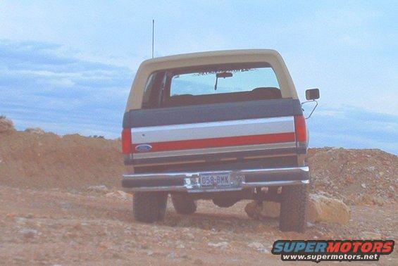 Rear view of a tan and dark blue 1989 Ford Bronco with red and silver stripes on tailgate