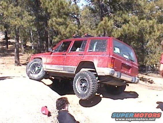 Red Jeep Cherokee XJ with lifted suspension and off-road tires on uneven terrain