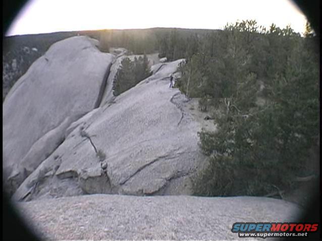 person standing on a large rock formation with trees and a sunset in the background