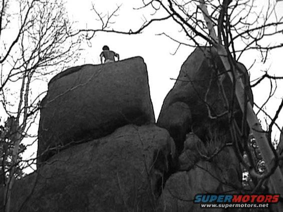 Person atop large rock formation with bare tree branches overhead