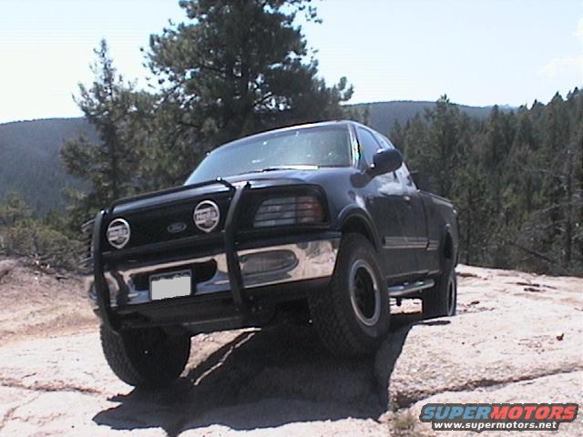 Black Ford F-150 pickup truck with bull bar driving on rocks