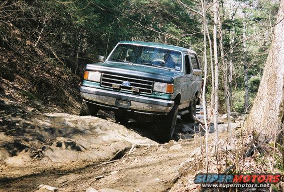 Green Ford Bronco driving over rocks on a dirt trail