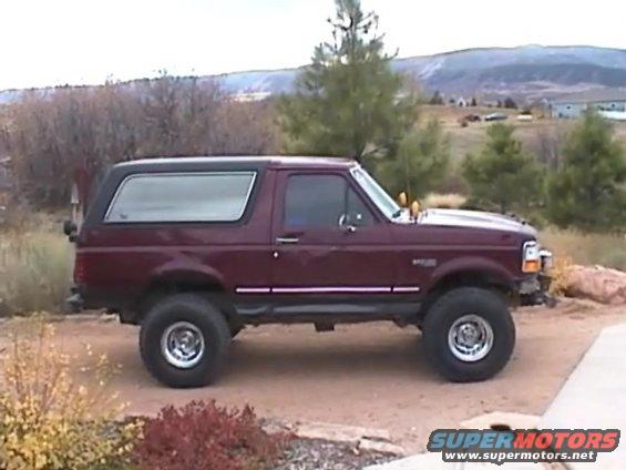 Maroon Ford Bronco with black top, lifted suspension, and aftermarket wheels parked on a dirt lot