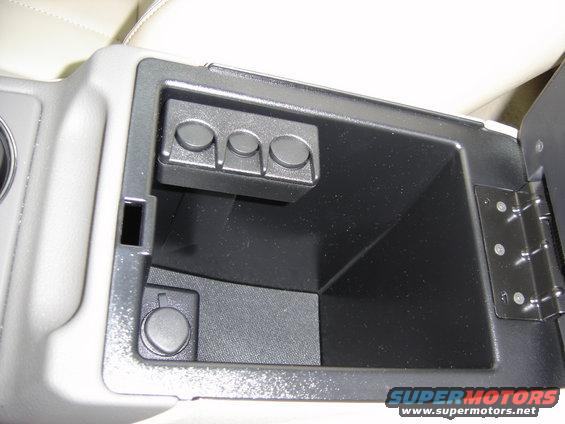 car's open center console with three circular buttons and a 12v power outlet