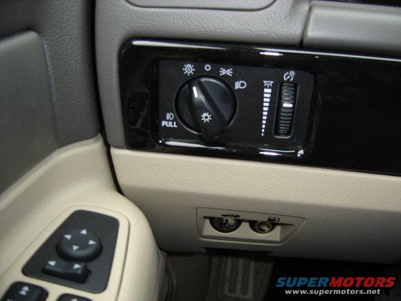 Car interior showing headlight controls, dimmer switch, and power outlets