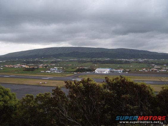 Airport scene with distant buildings and a mountain under a cloudy sky