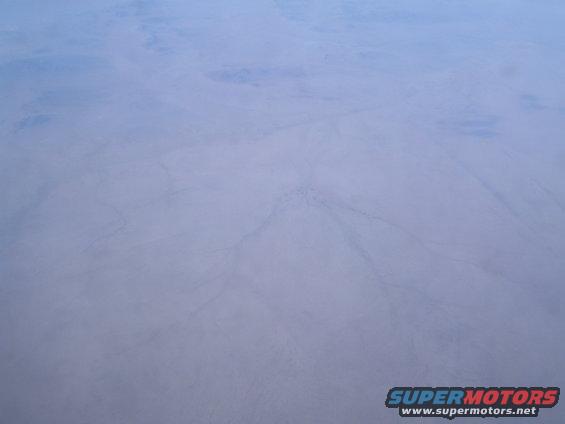 Aerial view of a vast, arid desert with faint tracks visible on the dusty ground
