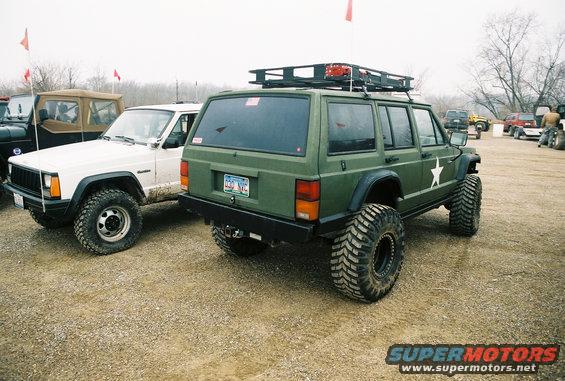 Green Jeep Cherokee XJ with large tires and roof rack parked next to a white Jeep Cherokee XJ